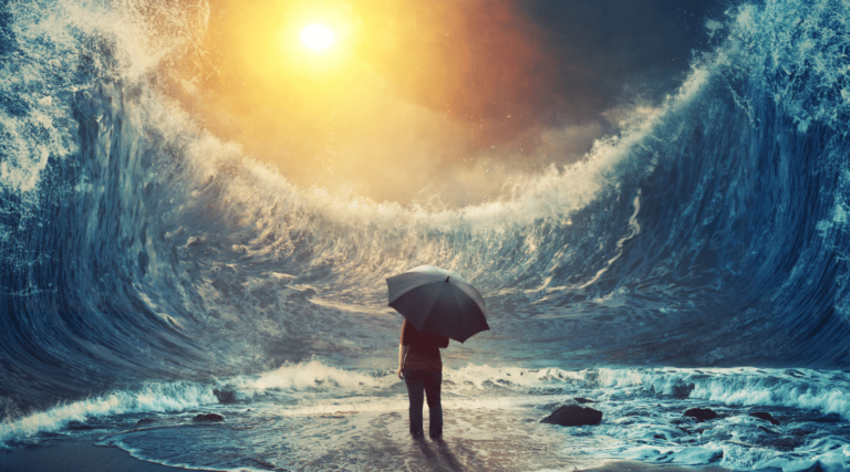 person stands on the beach holding up an umbrella whilst a giant tidal wave surrounds them